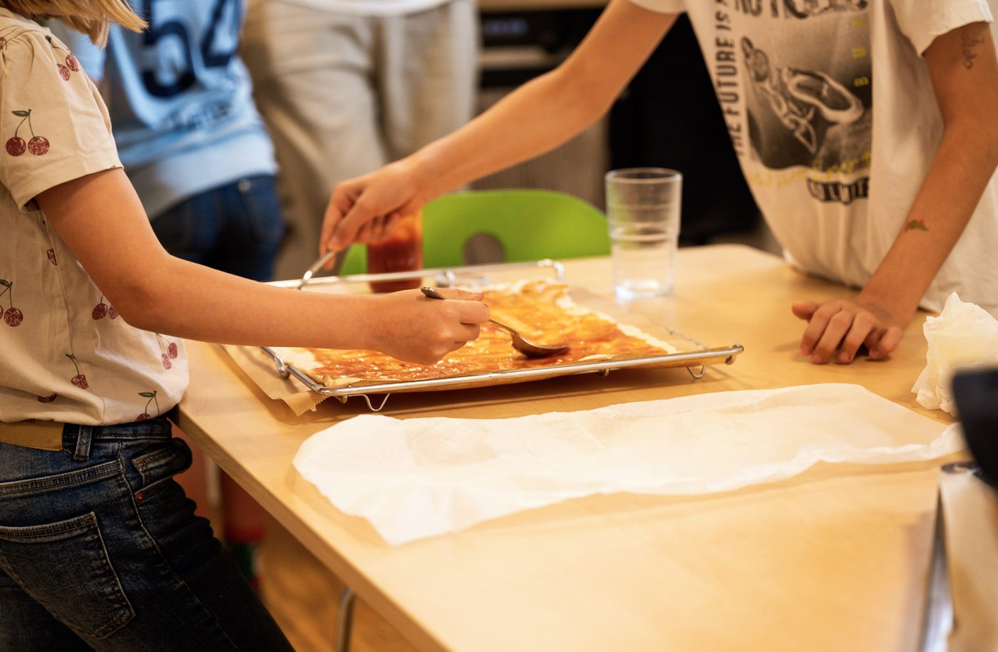 Kinder bestreichen Pizzateig mit Tomatensauce beim Pizzabacken